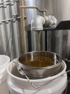 Oil being filtered through a metal sieve into a white bucket in an industrial setting.